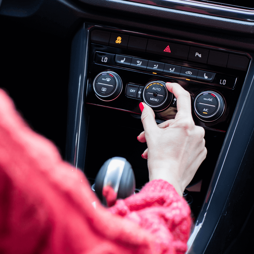 A lady in the driver's seat of a Volkswagen vehicle configuring the air conditioning console of the vehicle.