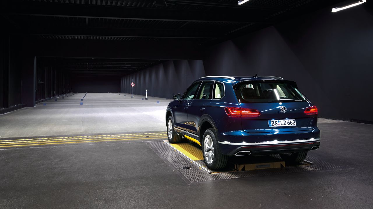 A parked dark blue Volkswagen SUV with its headlights switched on in a minimally illuminated empty building.