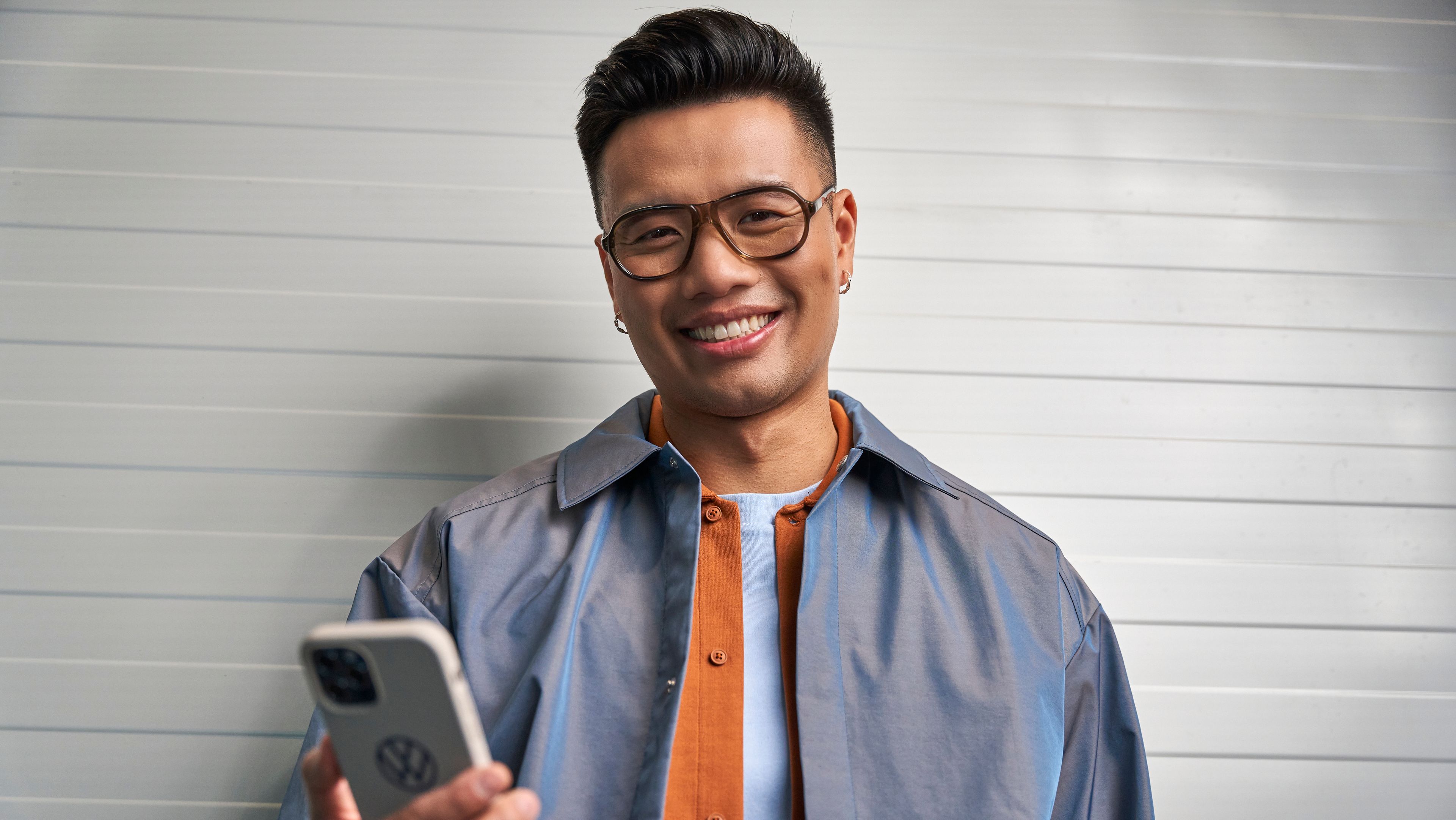 An asian guy smiling widely against a grey background with a phone in his hand