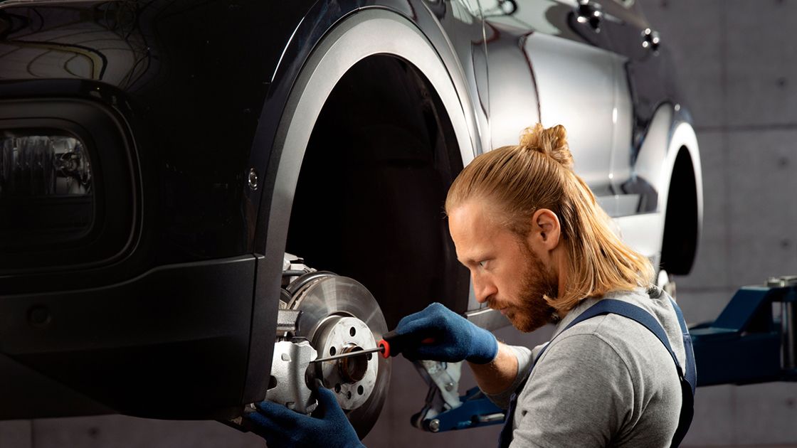 A Certified Volkswagen Technician repairing the brake disc and pad of a Volkswagen vehicle in a workshop.