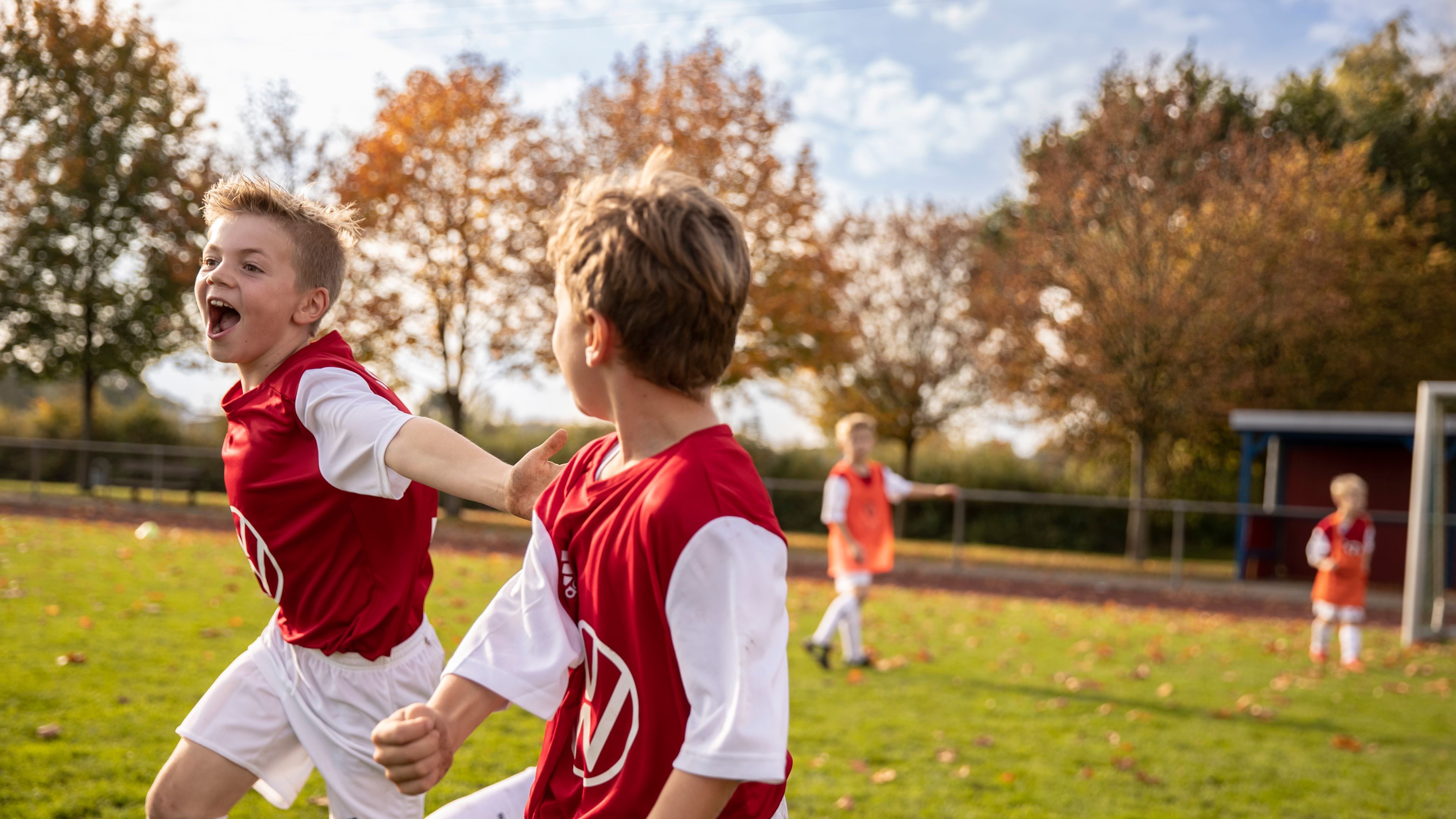 Kids dressed in red Volkswagen jerseys are seen playing football at an outdoor field.