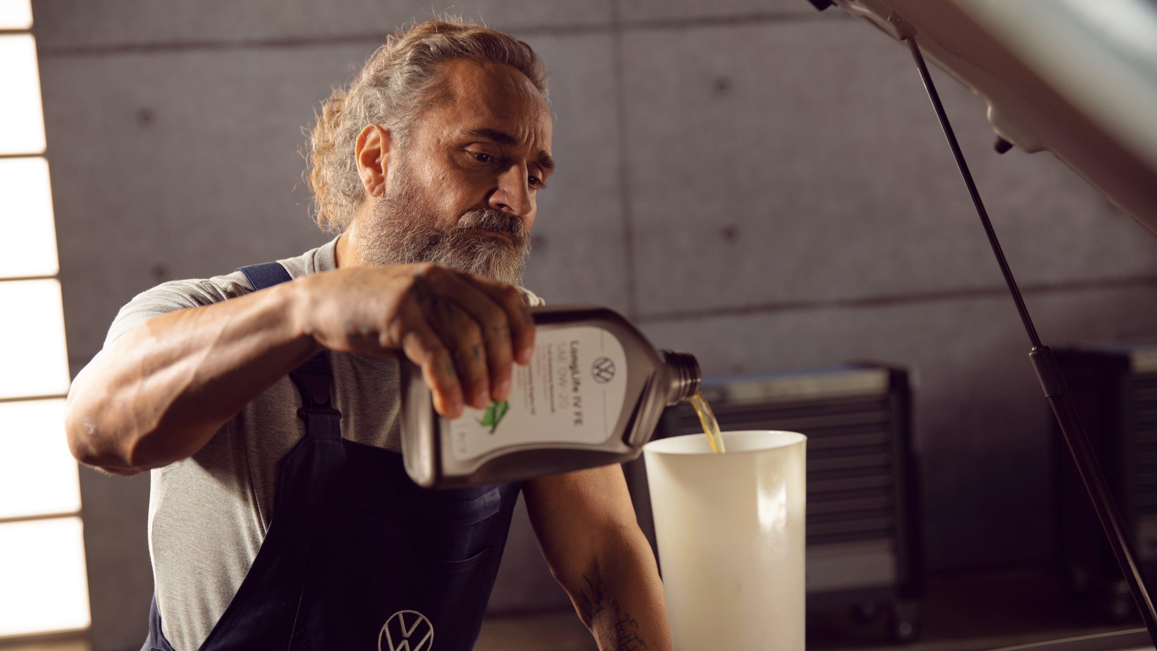 A Certified Volkswagen Staff pouring a Volkswagen approved engine oil into the engine of a Volkswagen vehicle using a white filter funnel.
