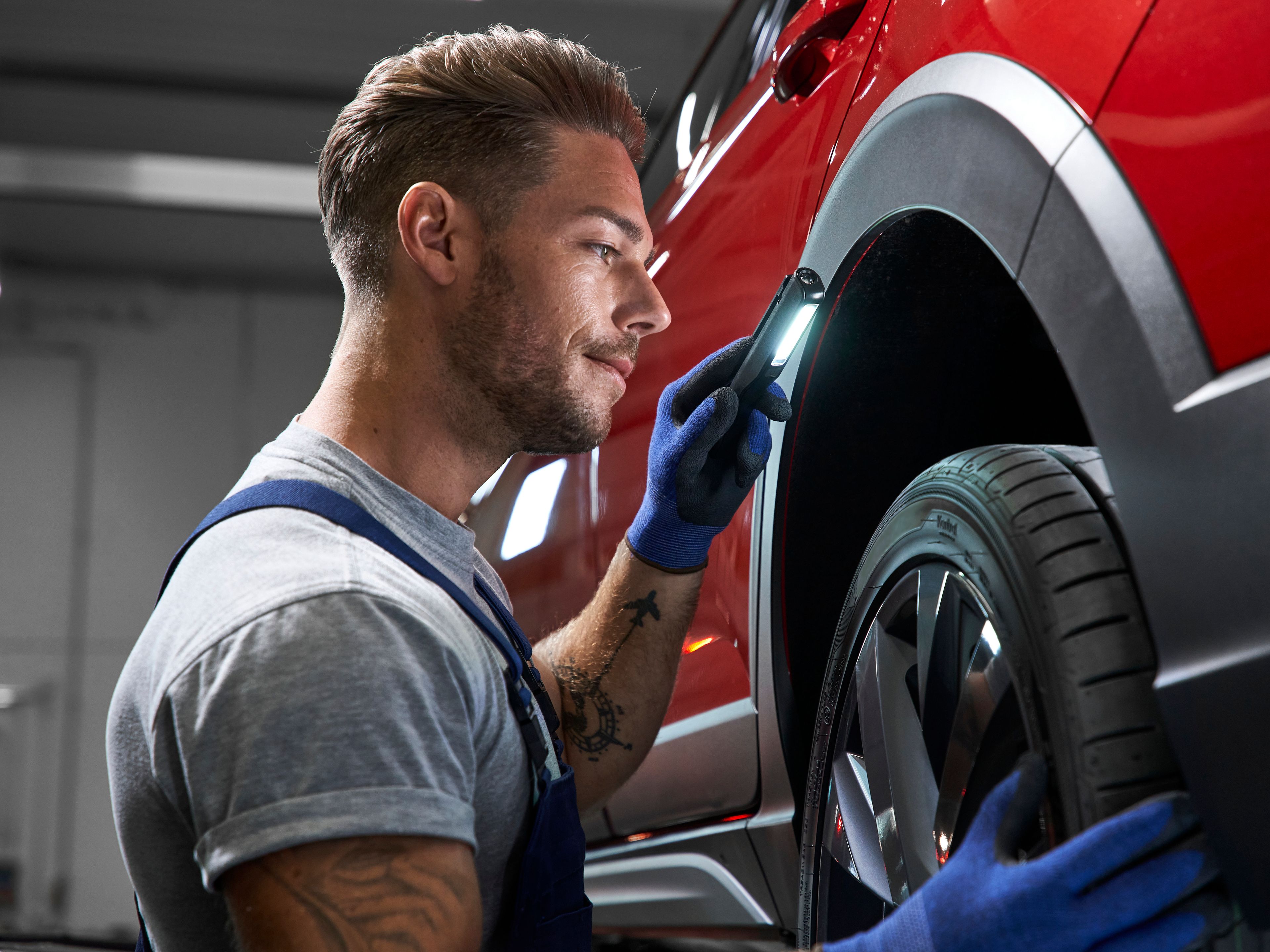 A Volkswagen technician inspecting the tyre of a red Volkswagen vehicle.