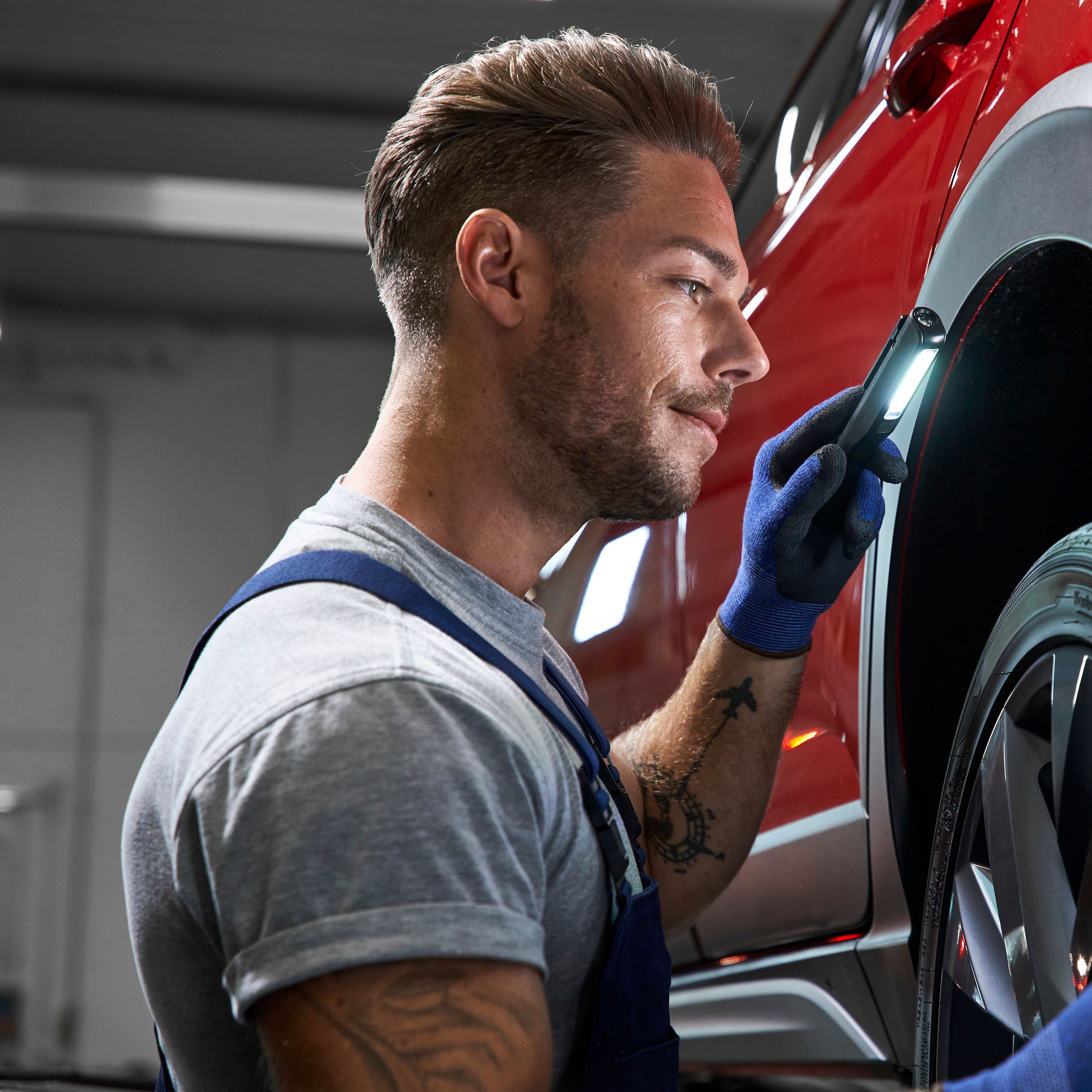 A Volkswagen technician inspecting the tyre of a red Volkswagen vehicle.