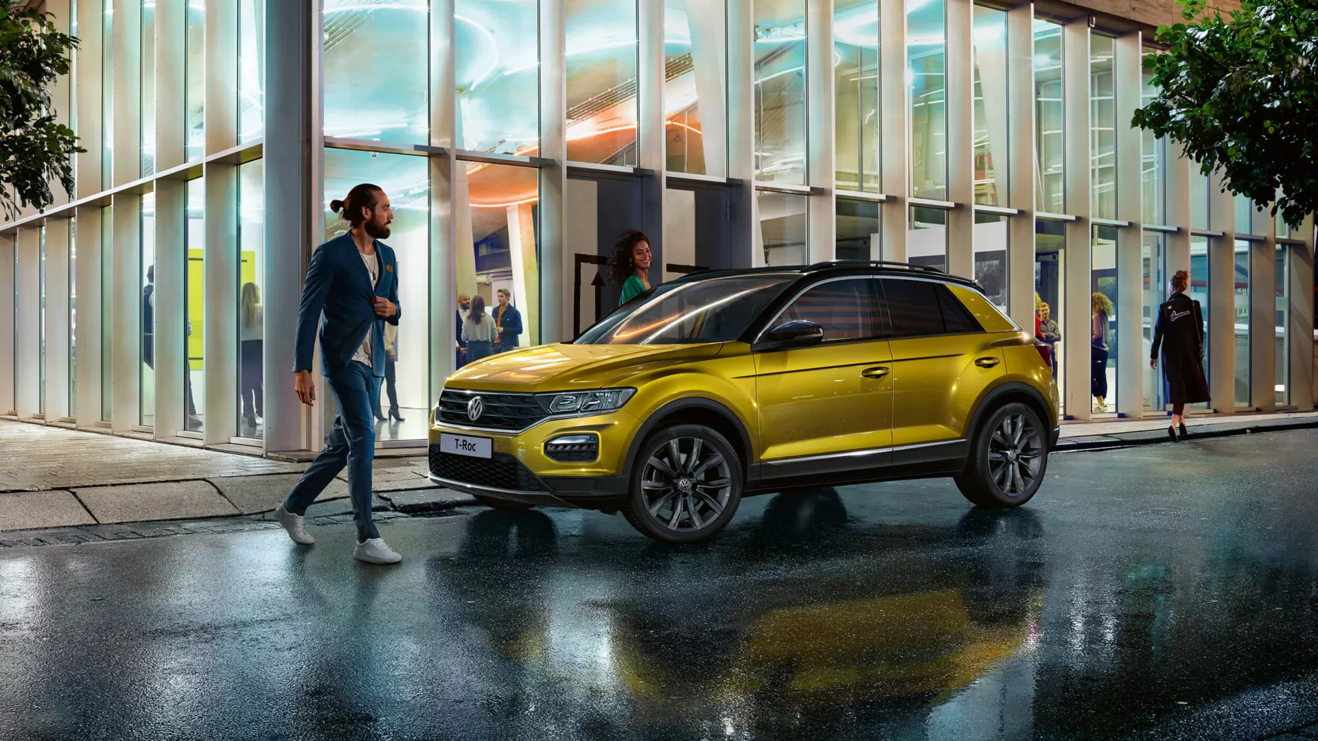 An individual crossing the road while a yellow Volkswagen vehicle is parked beside a building at an outdoor urban setting under a rainy weather.