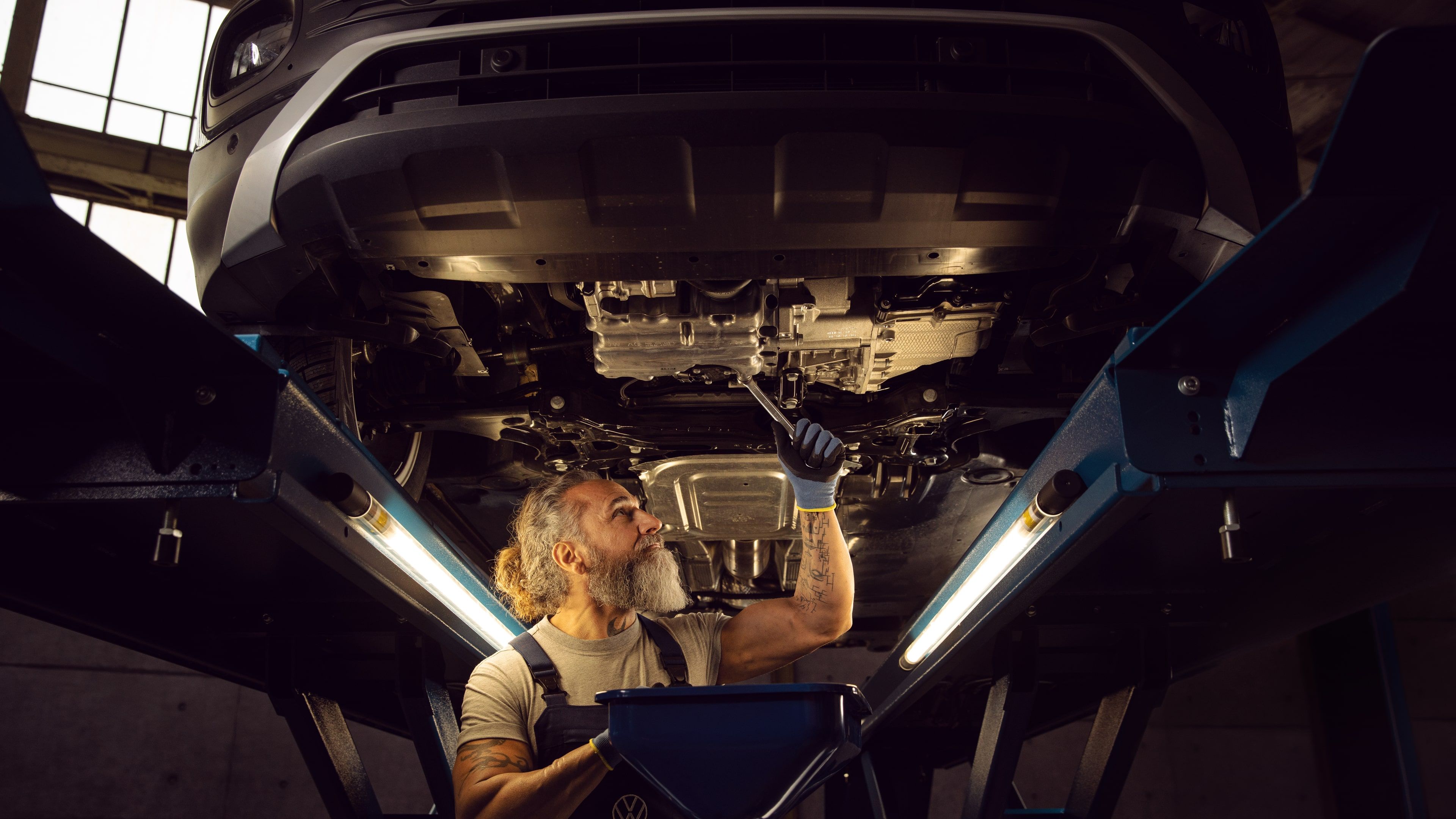A Certified Volkswagen mechanic using a wrench to tighten or fix a part of the undercarriage of a Volkswagen vehicle in a service workshop.