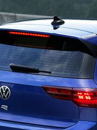 A blue Volkswagen Golf R-line with the rear headlight switched on at the hillroad beside the mountain