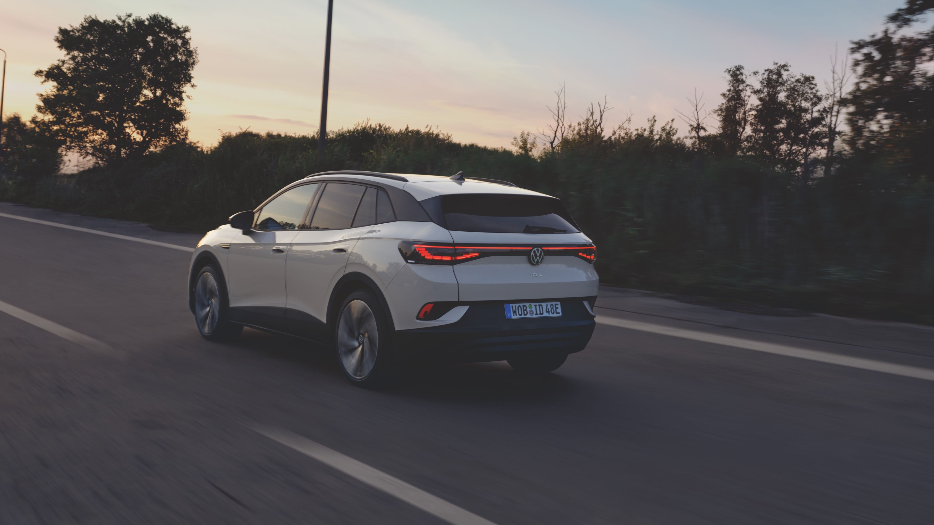 A white Volkswagen ID.4 driving down a clear highway at dusk.