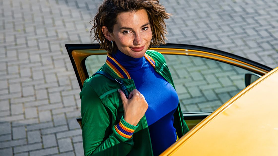 A chic looking lady smiling beside a yellow Volkswagen vehicle with its driver door opened.