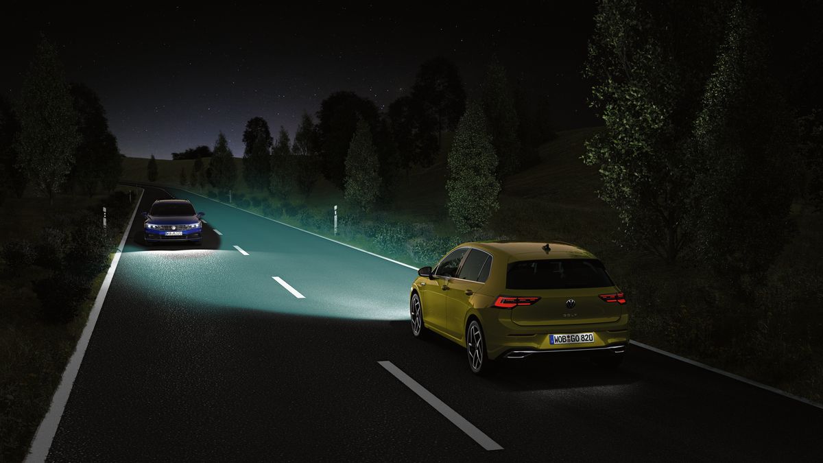 An image of a yellow Volkswagen vehicle with its headlamps switched on with another incoming vehicle on an opposite direction of the road at night.