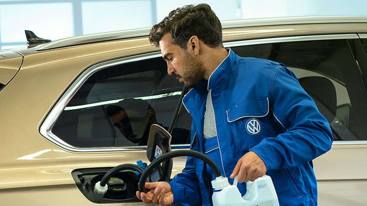 A Certified Volkswagen Technician filling AdBlue fluid into a Volkswagen vehicle.