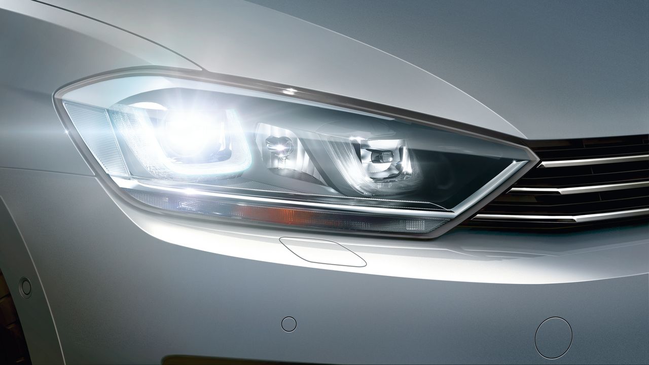A close-up look of a silver Volkswagen vehicle with its Bi-Xenon headlights switched on.