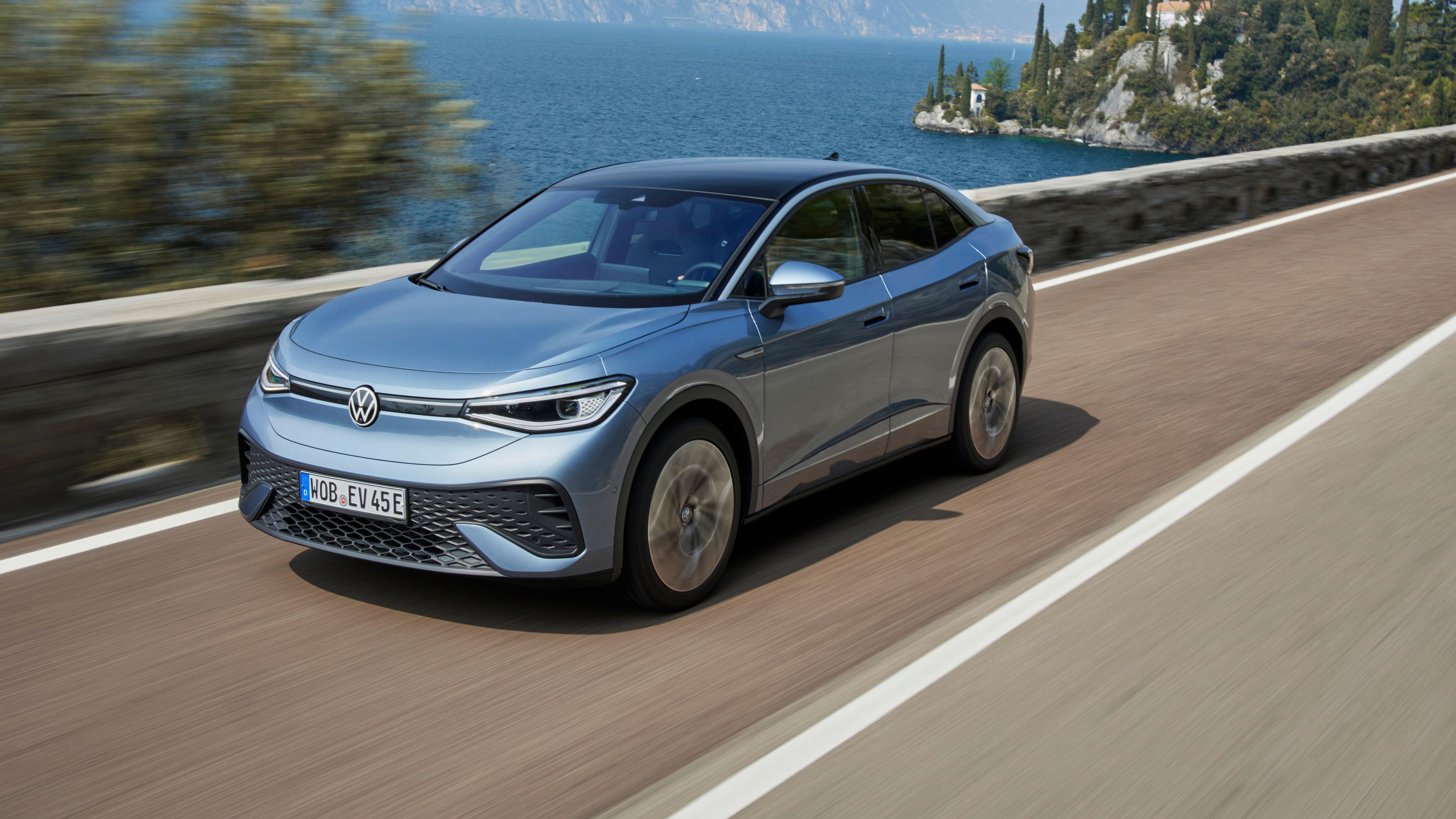 A Grey Volkswagen ID.5 is in motion in fast speed on the road beside the mountain