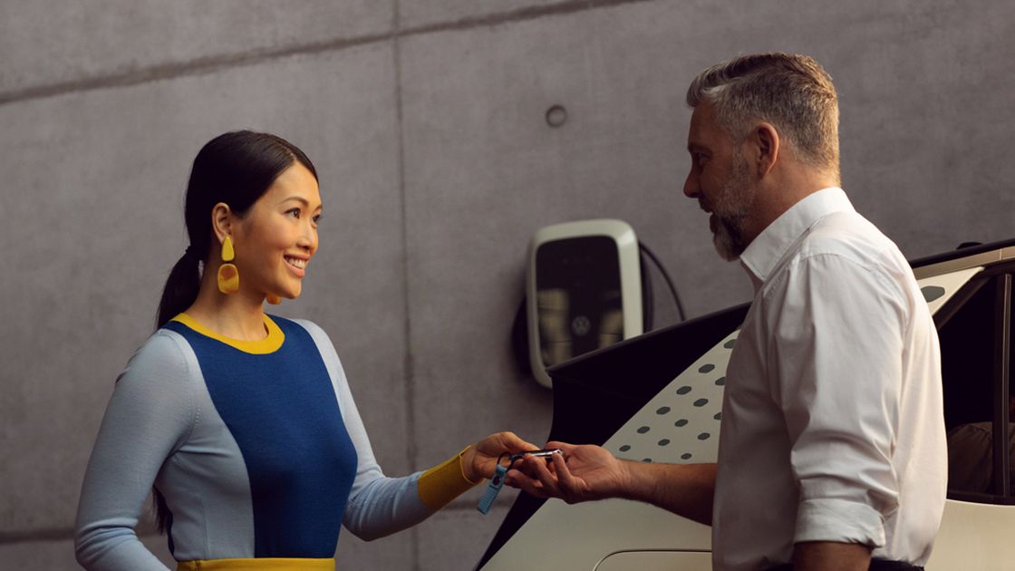 A Certified Volkswagen Staff handing over the car key to a Volkswagen Owner in a service workshop.