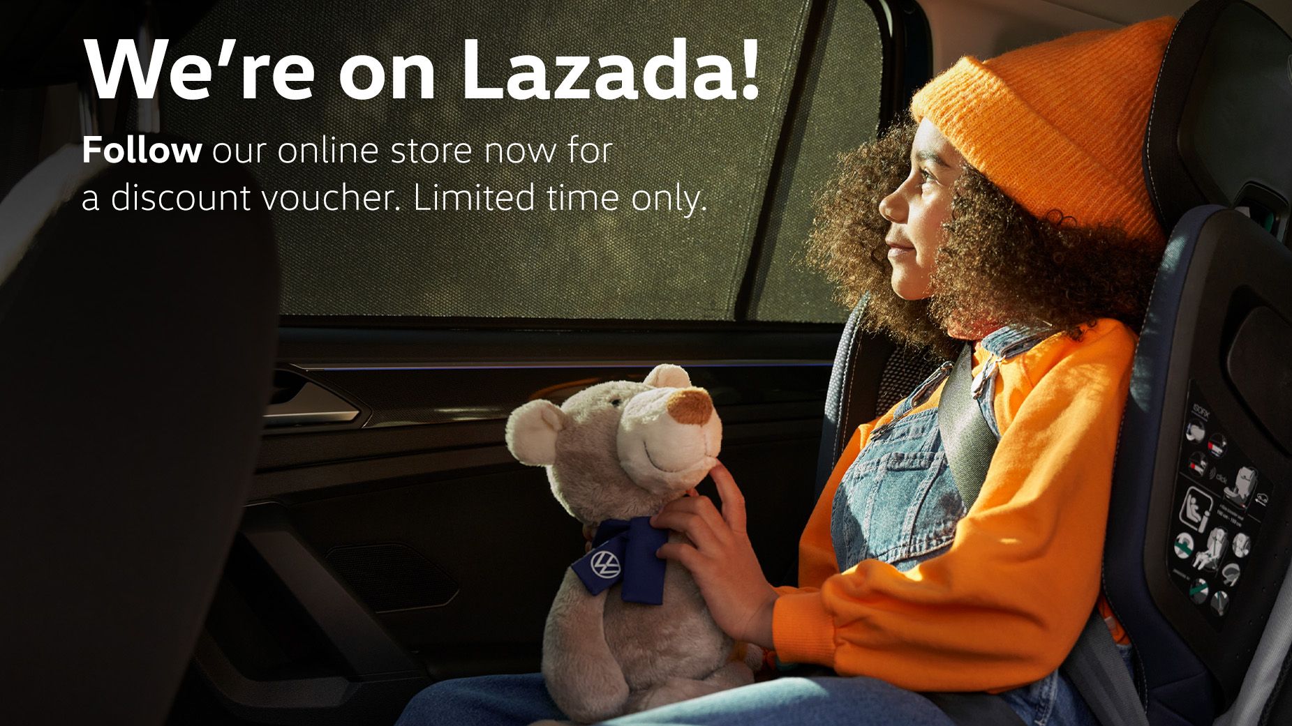 A kid sitting at the backseat of a Volkswagen vehicle holding a plush teddy bear looking out the window.