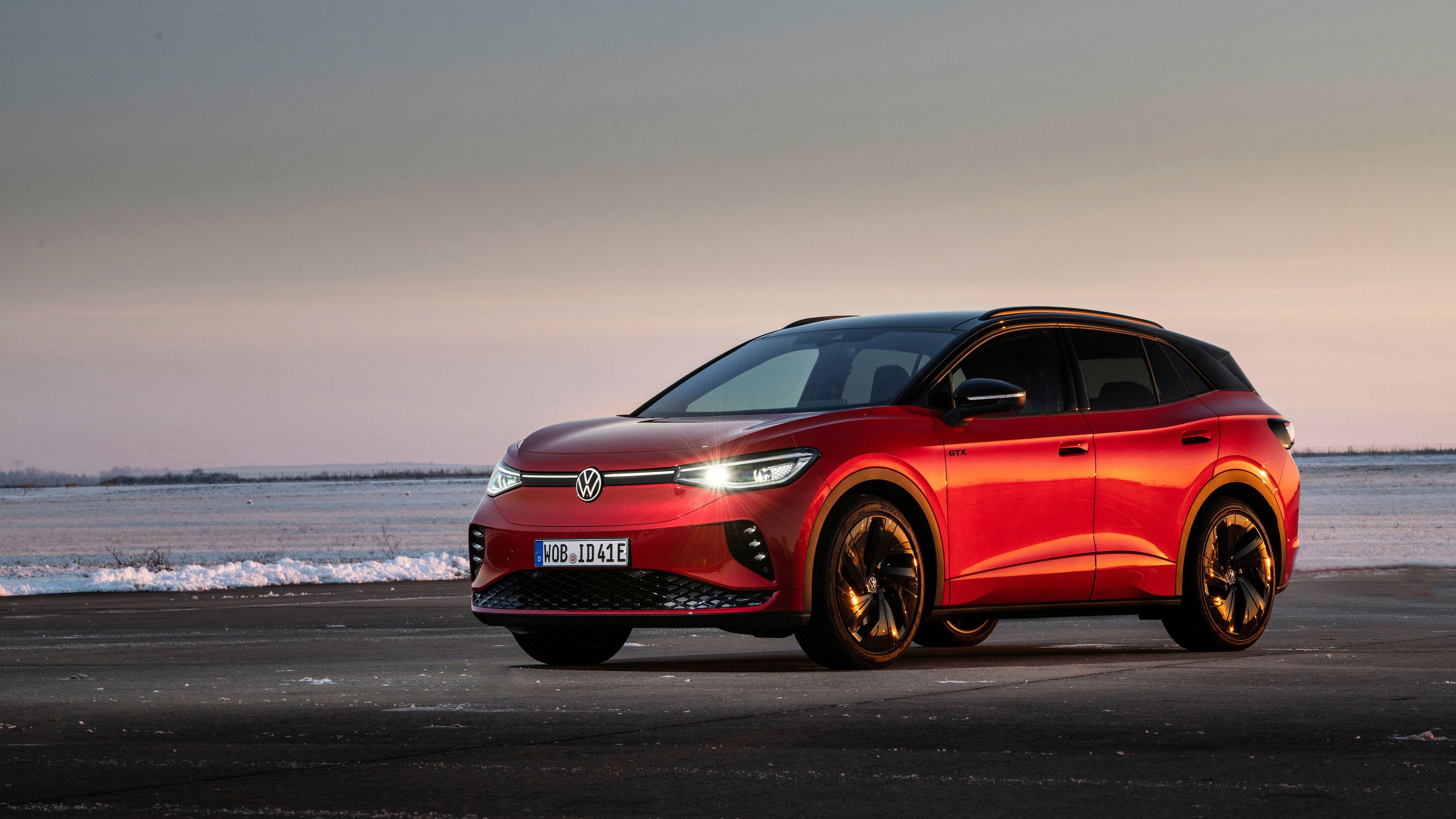 In a serene backdrop, Kings Red Premium Metallic Volkswagen ID.4 GTX is parked next to a large body of water with slight waves.