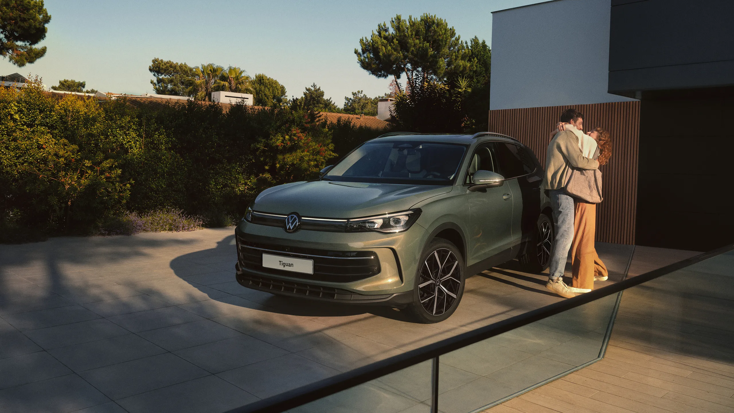 A metallic green Volkswagen Tiguan parked outside a residential home alongside a couple.