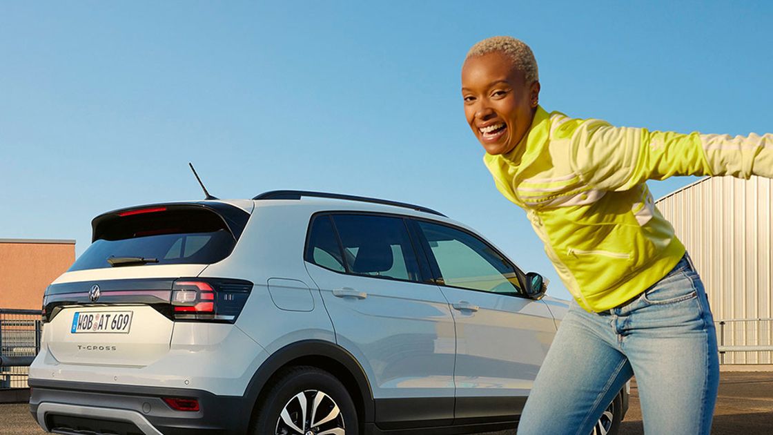 A chic lady jumping happily in front of a parked white Volkswagen SUV at an outdoor setting.