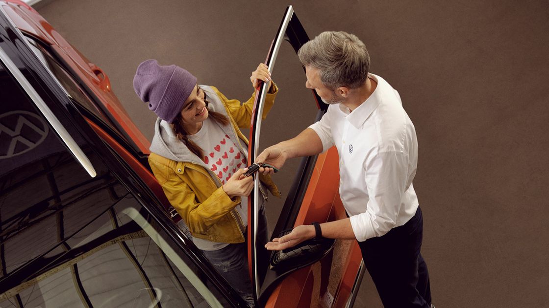 A Certified Volkswagen Staff handing over the car key to a young adult that is about to leave the service workshop.