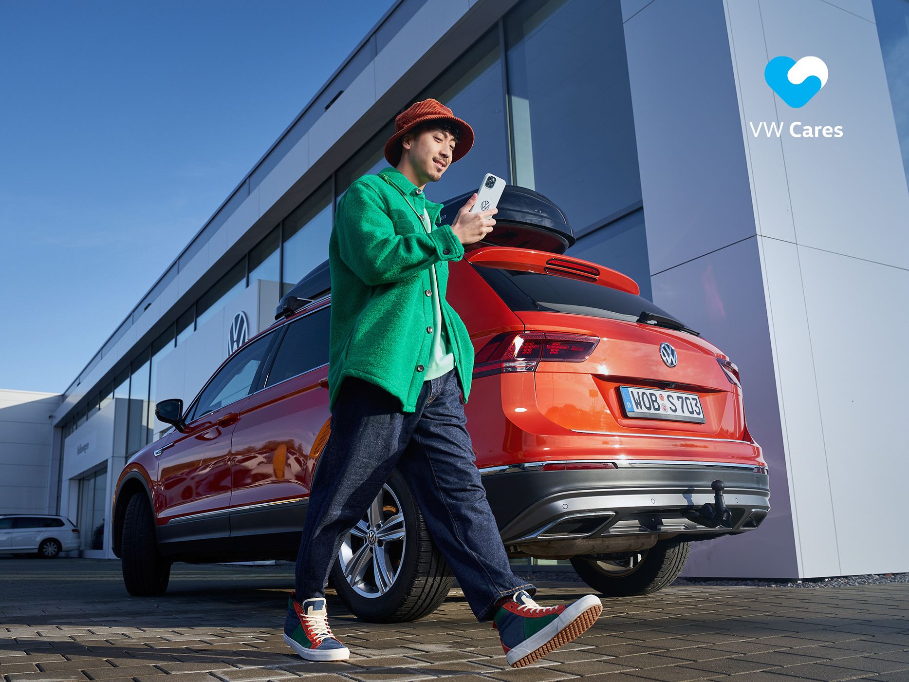 A man looking at his phone walking by a Volkswagen vehicle outside a building.