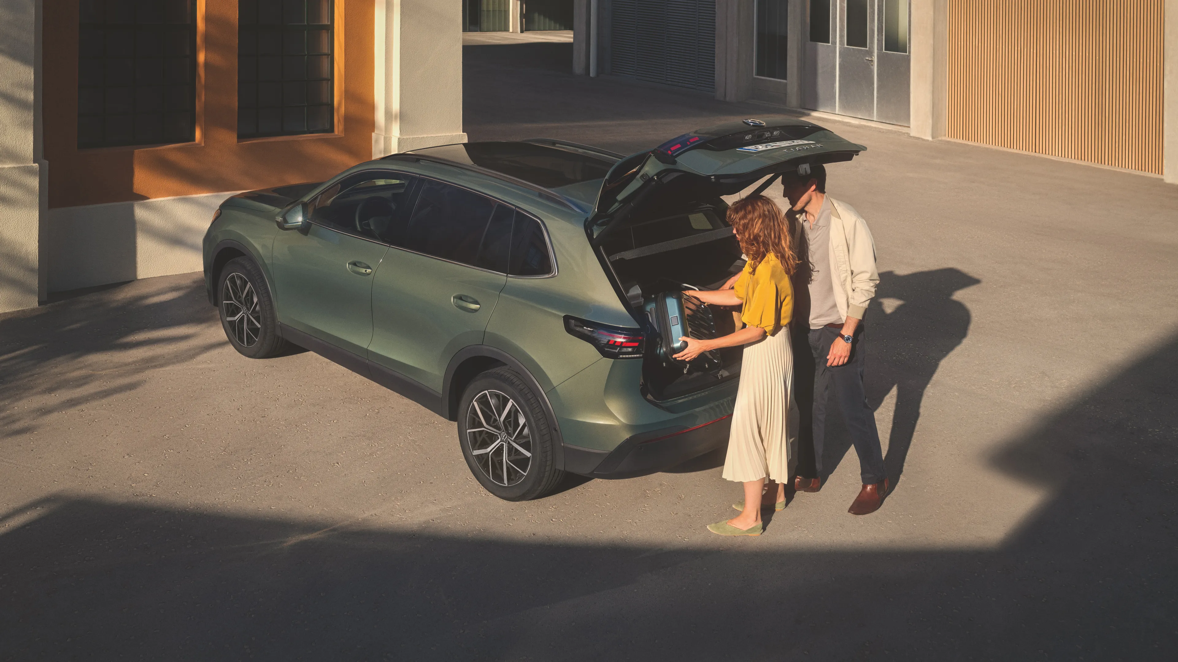 A couple putting the language on the boot space of a Volkswagen Tiguan parked in front of a building entrance.