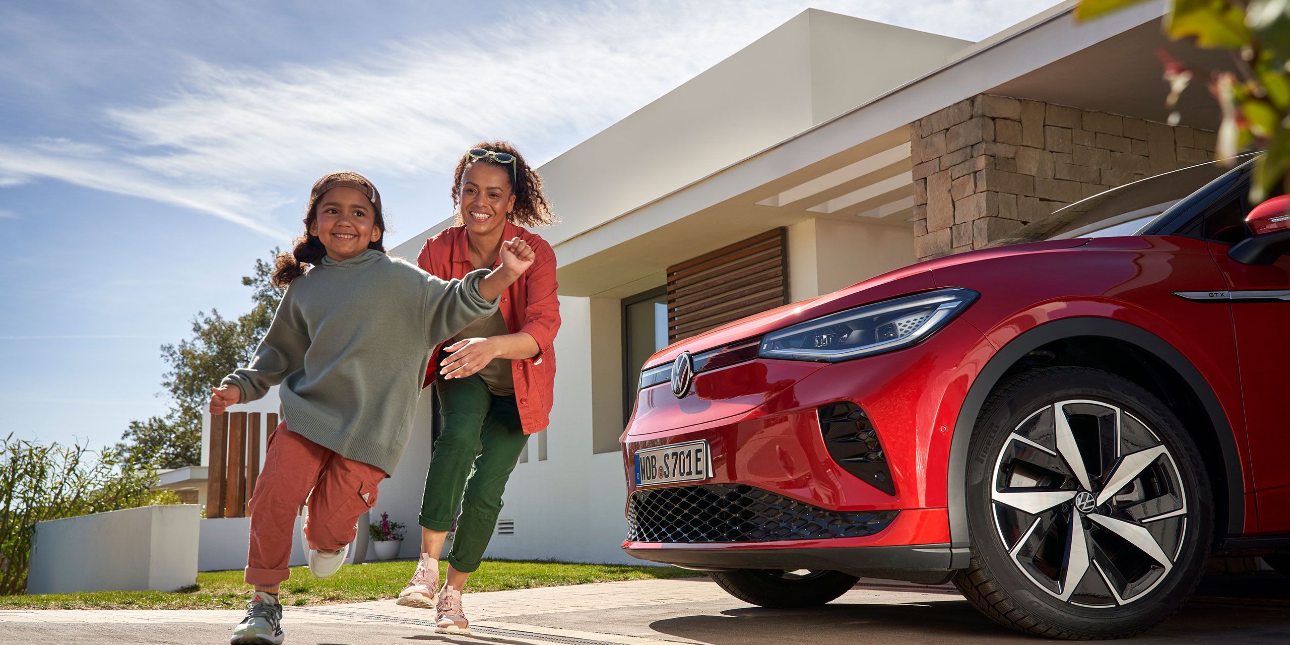 A women and her daughter is running infront the Volkswagen ID.4 GTX that parked beside a house.