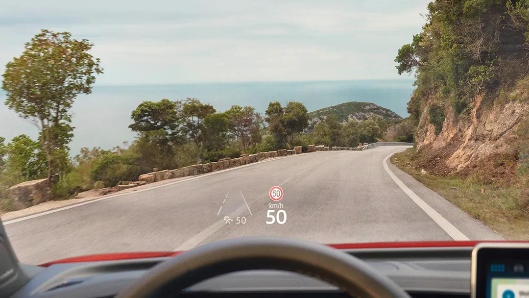 A person is seen using the Windshield Head-Up Display while driving on an open road.