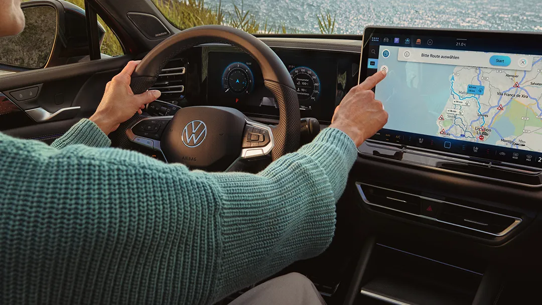 A lady dressed in a turquoise sweater is seen setting up the navigation system via the infotainment system of a Volkswagen Tiguan.