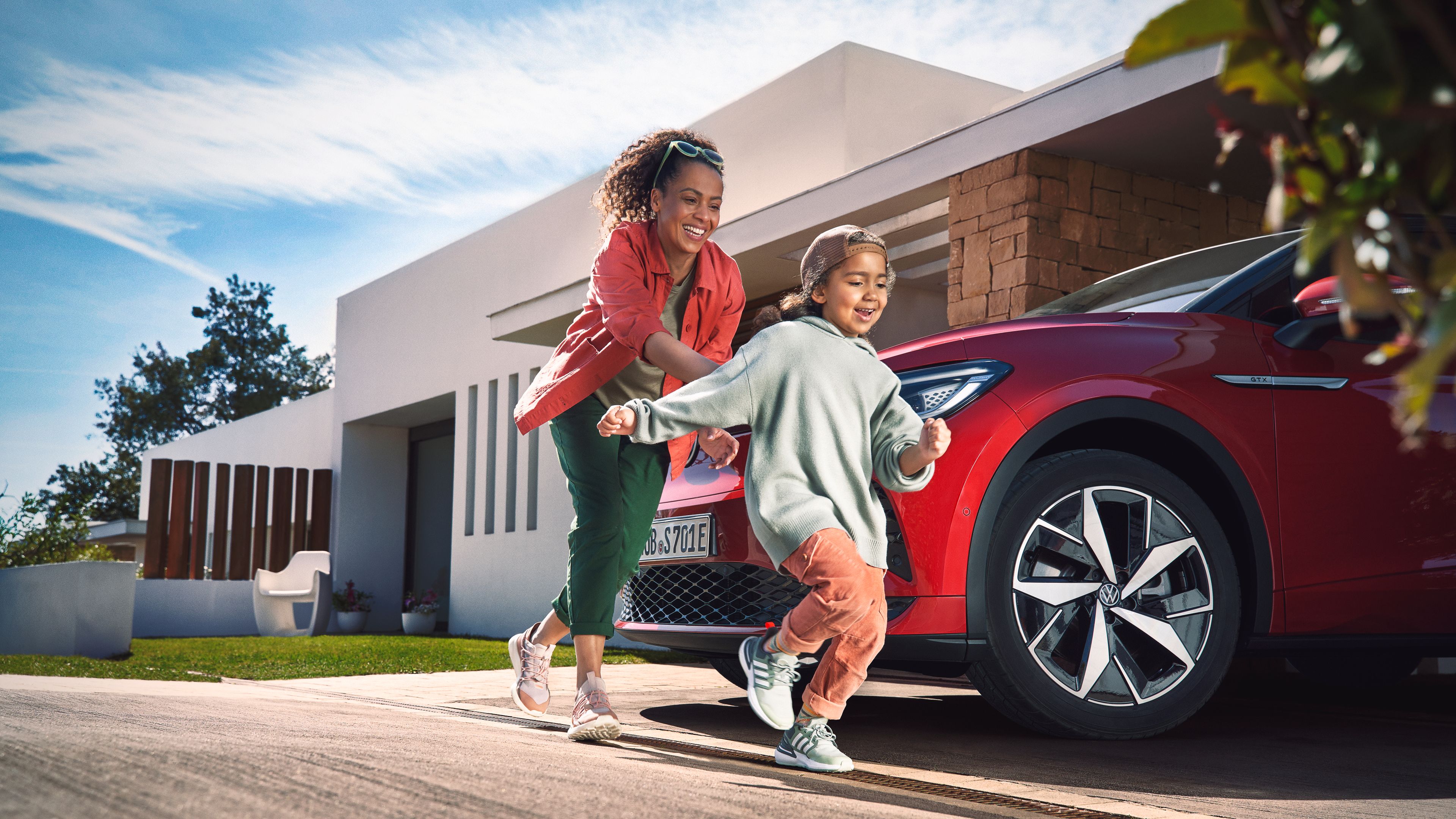 A mother is seen playing with her child in front of a parked Volkswagen ID.5 GTX at an outdoor setting.