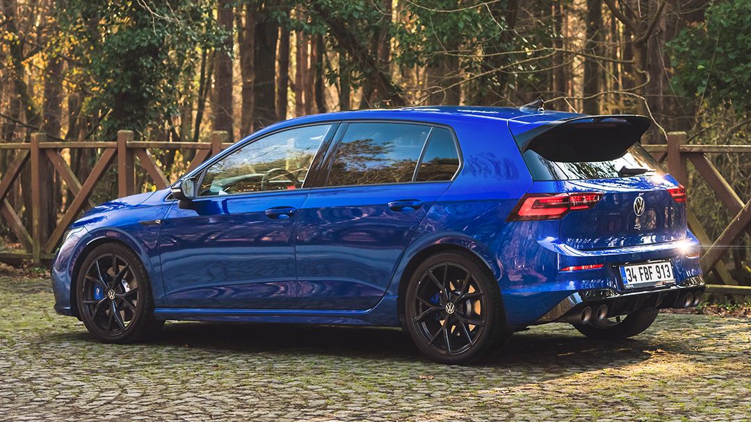 A blue Volkswagen vehicle in a cottage-like environment surrounded by autumn leaves and greenery