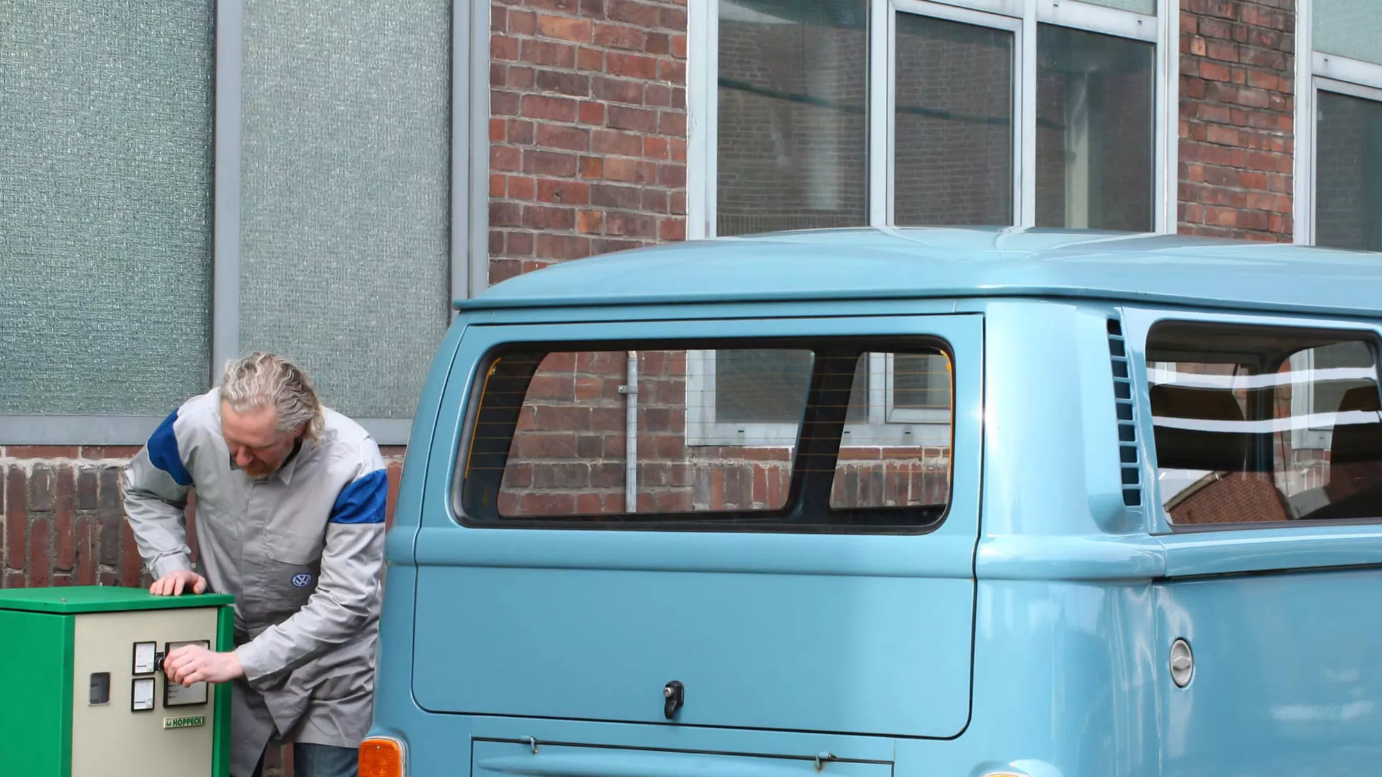 An old man is charging the blue T2 Elektor beside a house