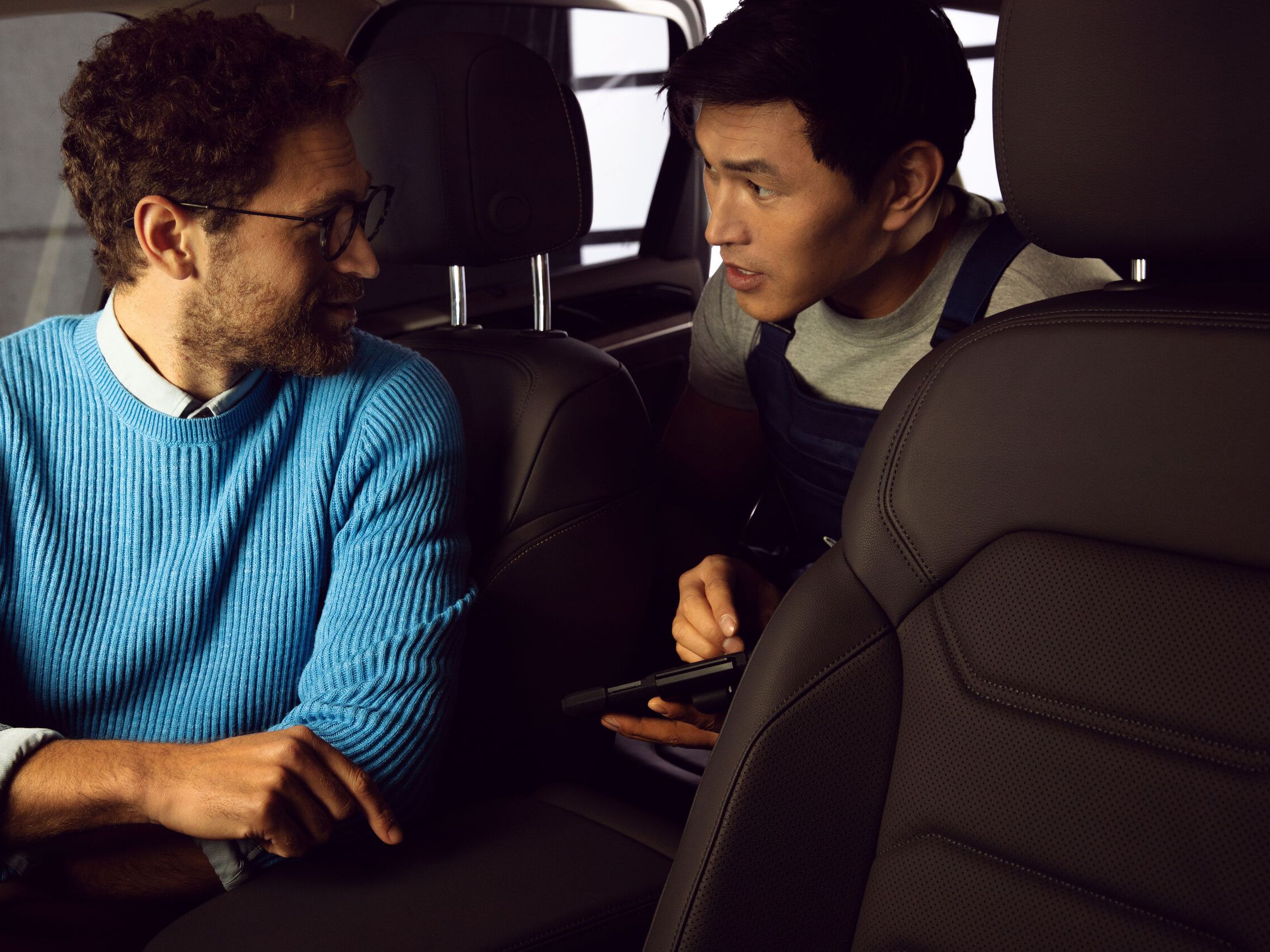 A man dressed in a blue sweater is seen talking to a service advisor inside a Volkswagen vehicle.