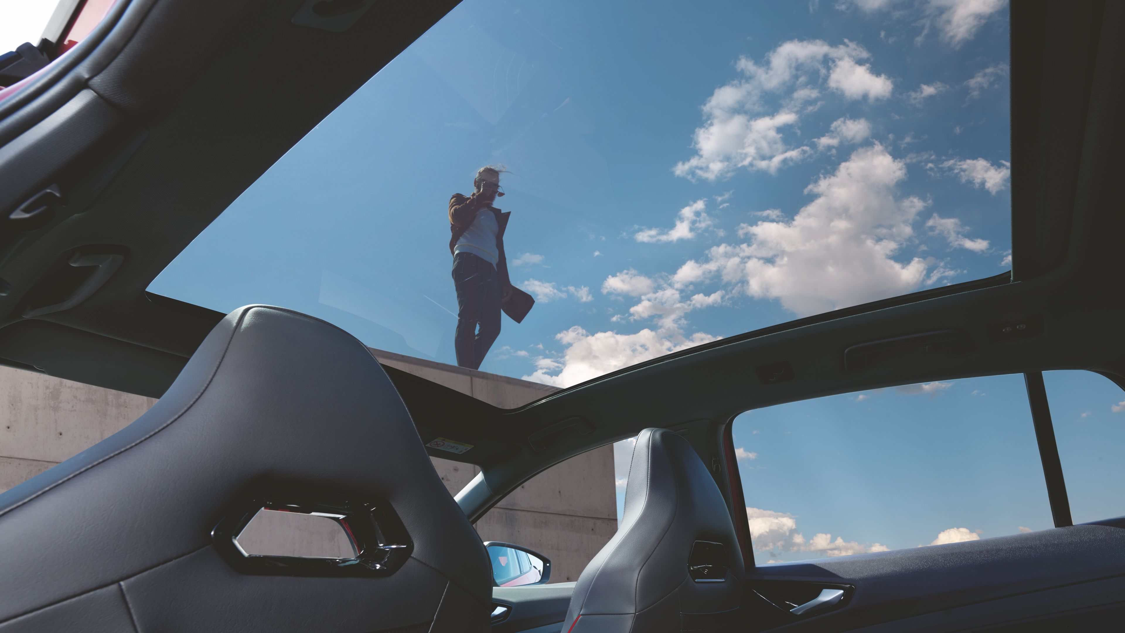 Shot from interior Volkswagen ID.5 GTX interior panoramic glass roof, man standing at the tall building