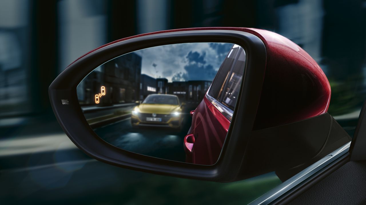 A close up image of a red Volkswagen vehicle's electric door mirrors with another vehicle in sight.