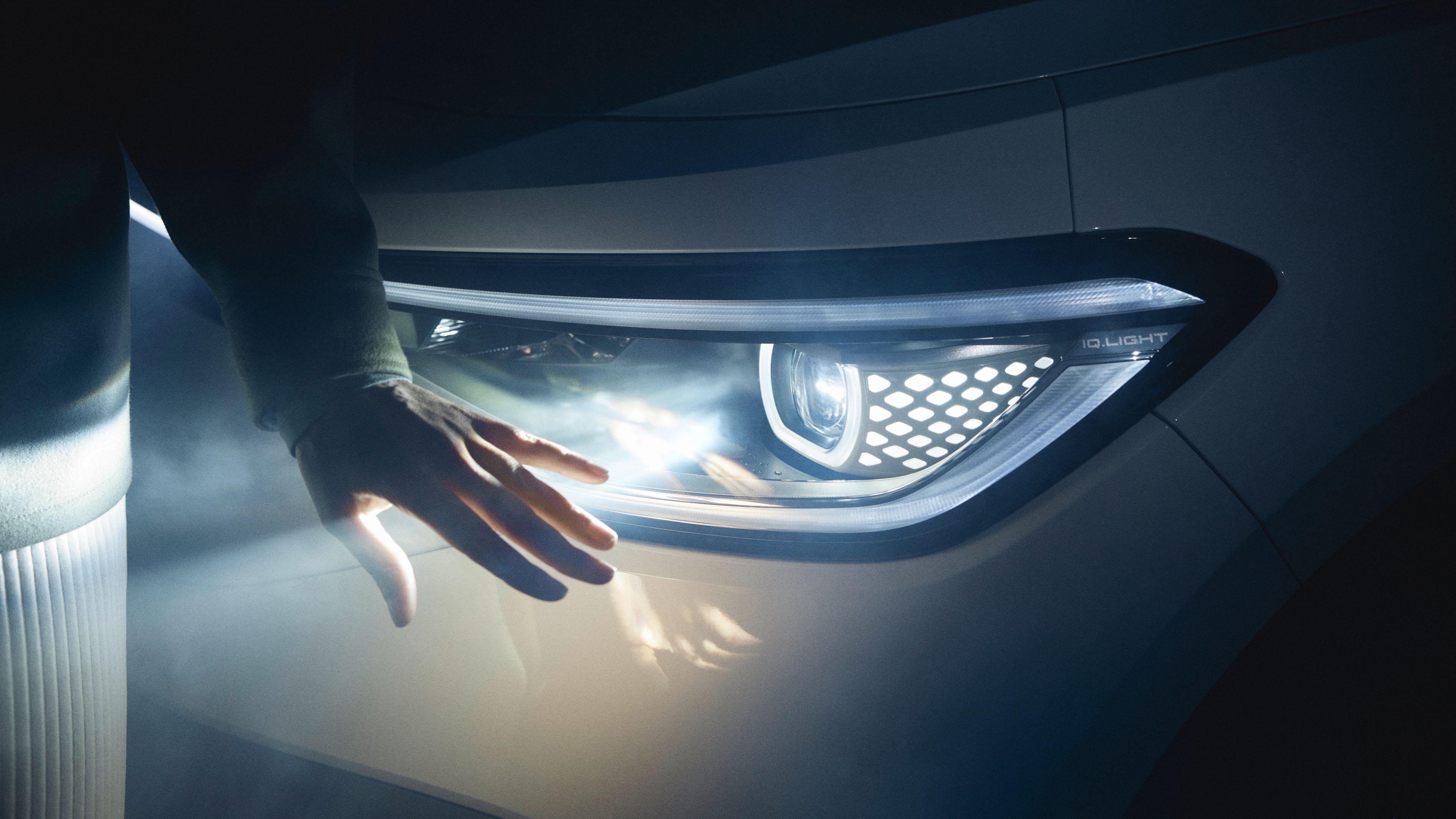 A person is trying to touch the headlights that turned on of Grey Volkswagen ID.5 in a dark space