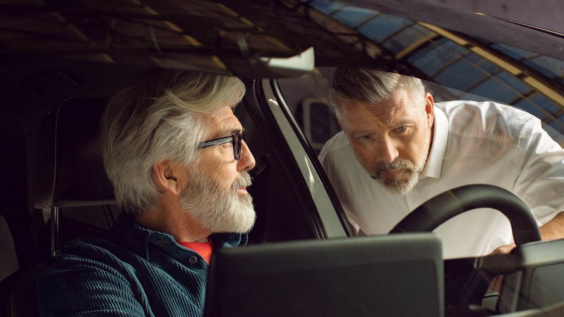 A Certified Volkswagen Staff guiding a Volkswagen Owner seated in the driver's seat of a Volkswagen vehicle on the vehicle's infotainment system.