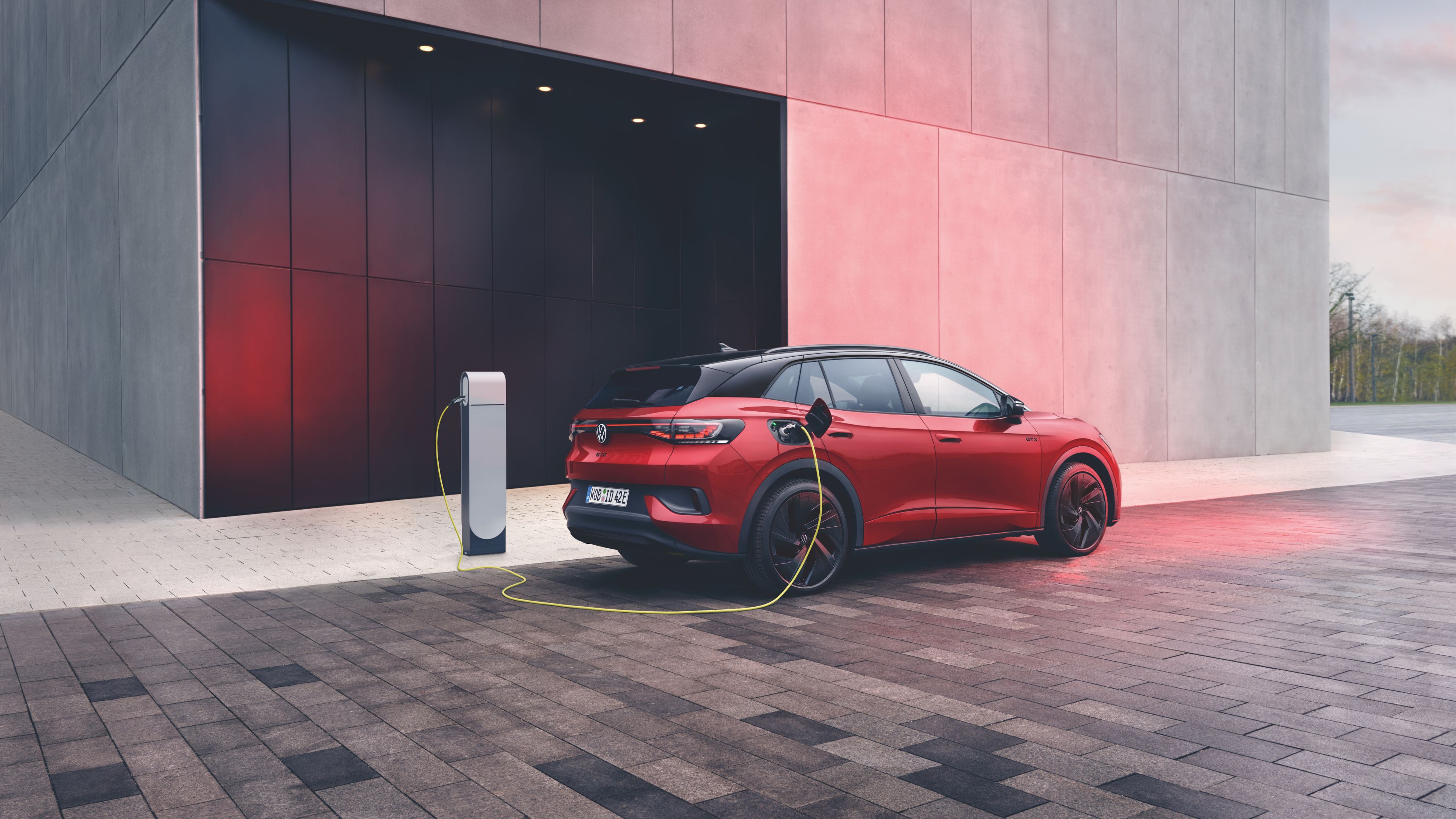 The Kings Red Premium Metallic Volkswagen ID.4 GTX is seen charging in front of a tall, grey corporate building.