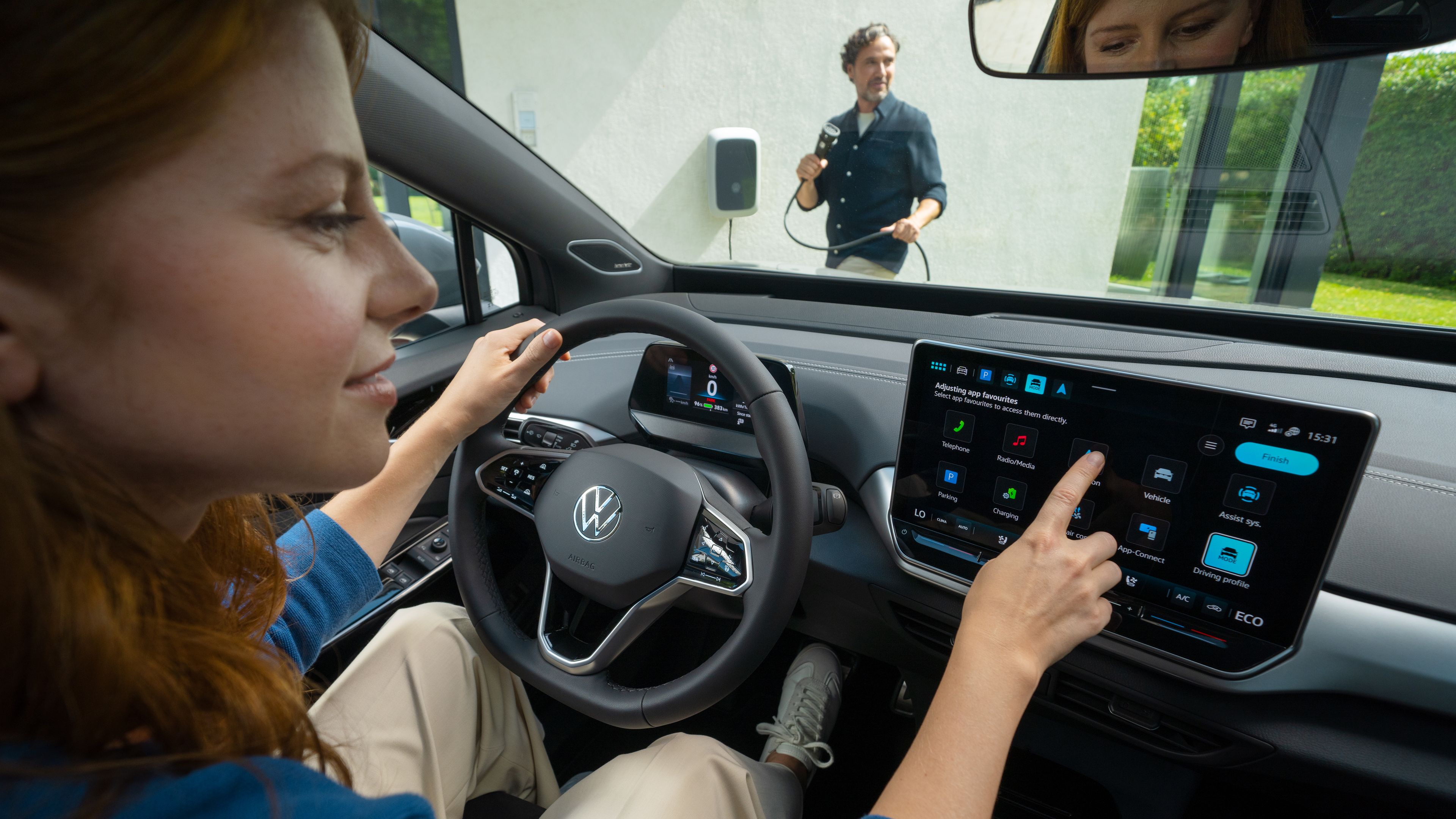 A lady in a blue shirt touching the Volkswagen ID.5 navigation system while a man wearing black holding the battery charger plug 