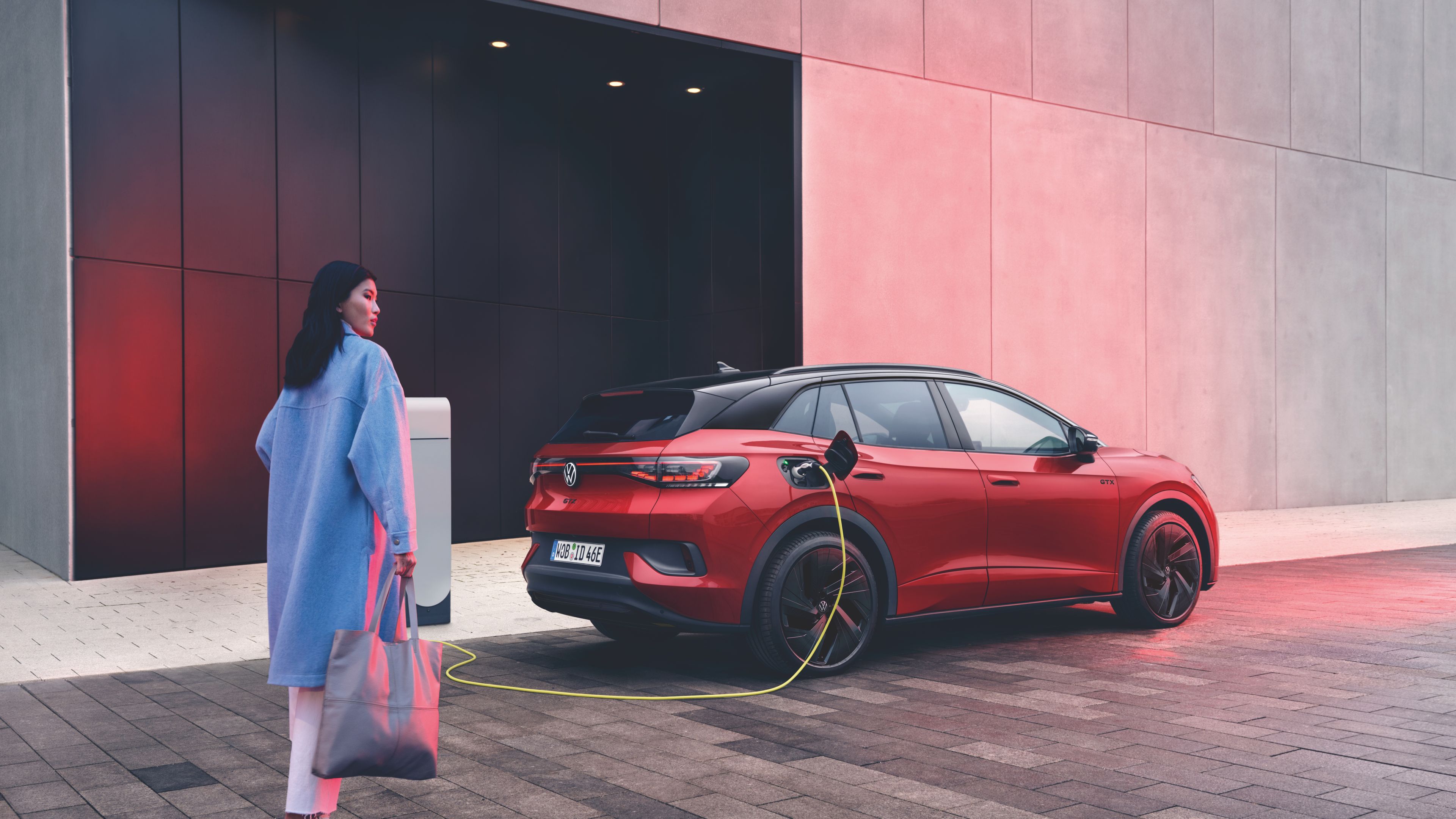 A lady in a blue coat walking towards the Volkswagen ID.4 GTX while it's charging.