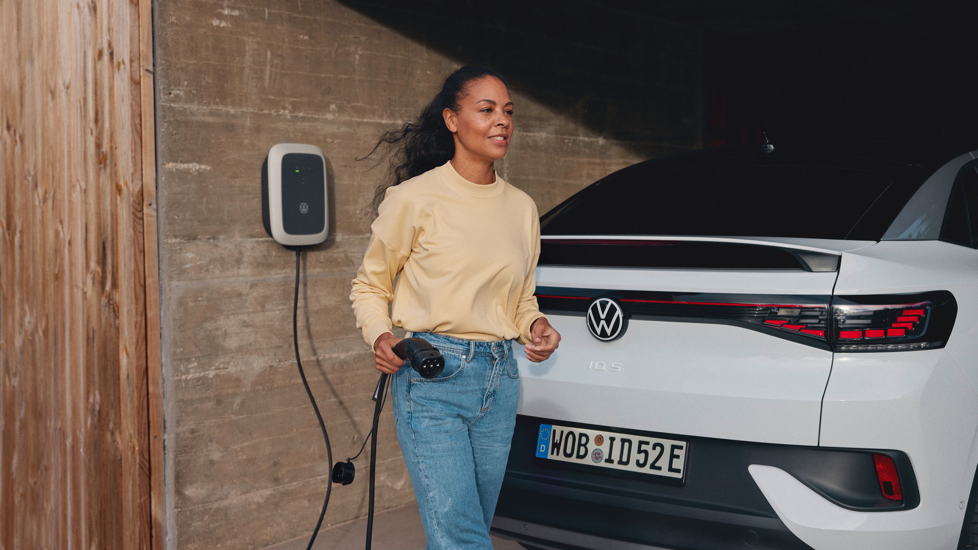 A lady dressed in casual outfit using an AC charger to charge a Pure White Volkswagen ID.5.