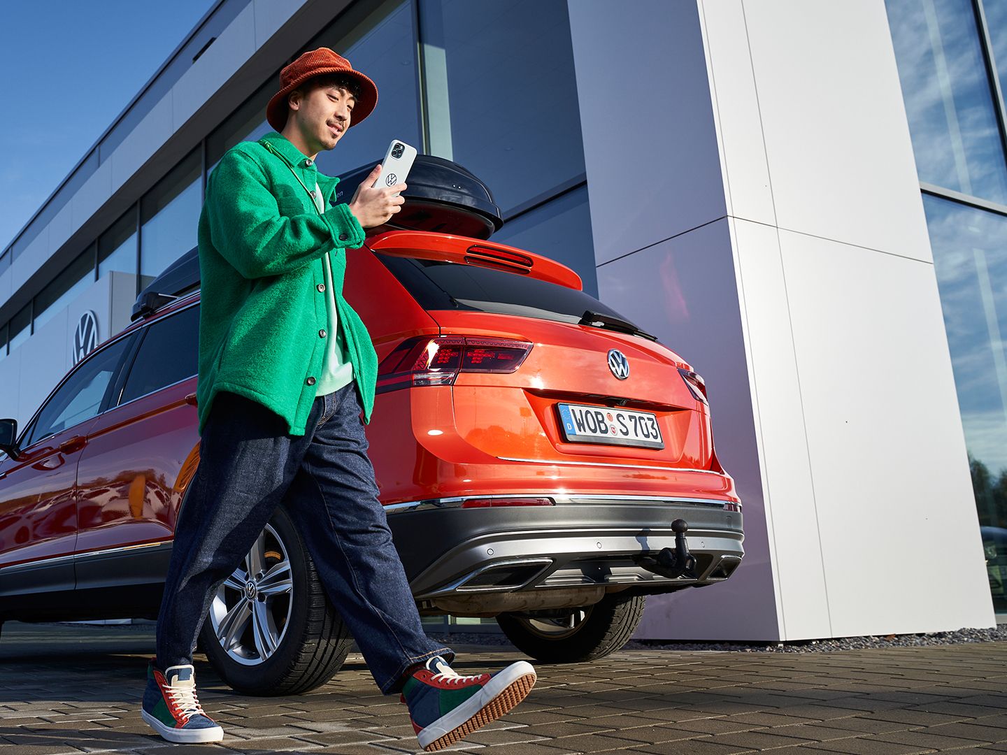 A man looking at his phone walking by a Volkswagen vehicle in the background