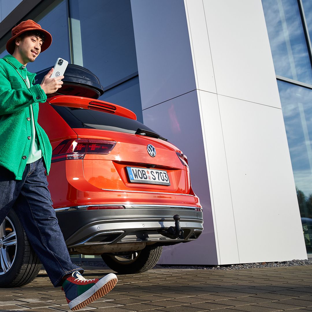 A man looking at his phone walking by a Volkswagen vehicle in the background