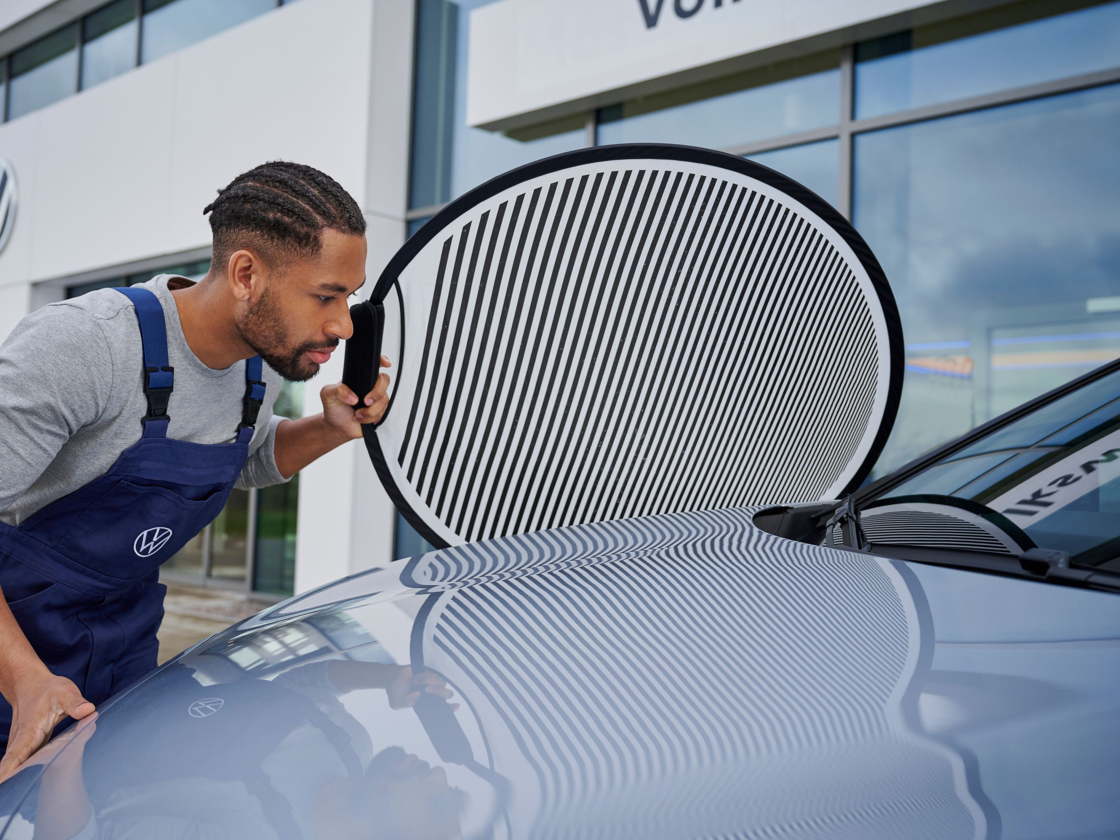 A Volkswagen technician inspecting the paint job finishing of a silver Volkswagen vehicle.