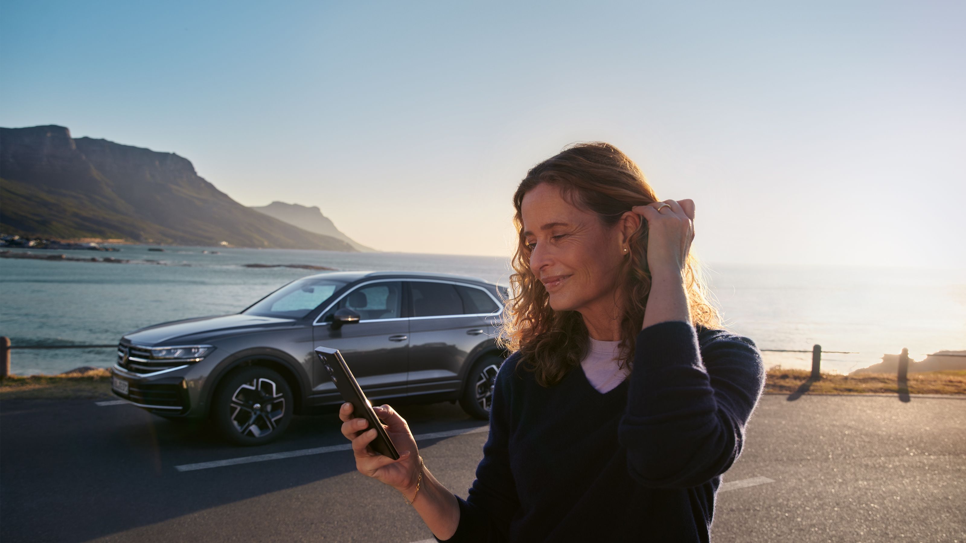 A lady looking at her phone with her vehicle against a scenic view