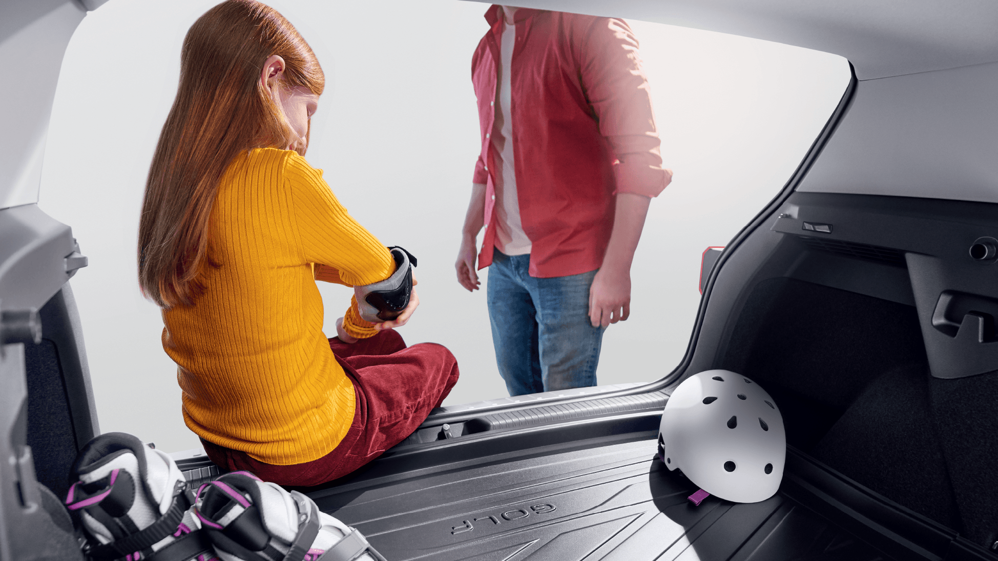 A kid sitting on the trunk of a Volkswagen vehicle while unstrapping her roller blading gears.