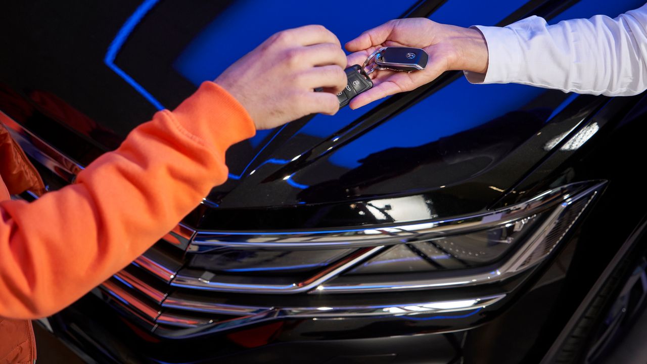 A Volkswagen owner handing over the car key to a Certified Volkswagen Staff for servicing over a black Volkswagen vehicle.