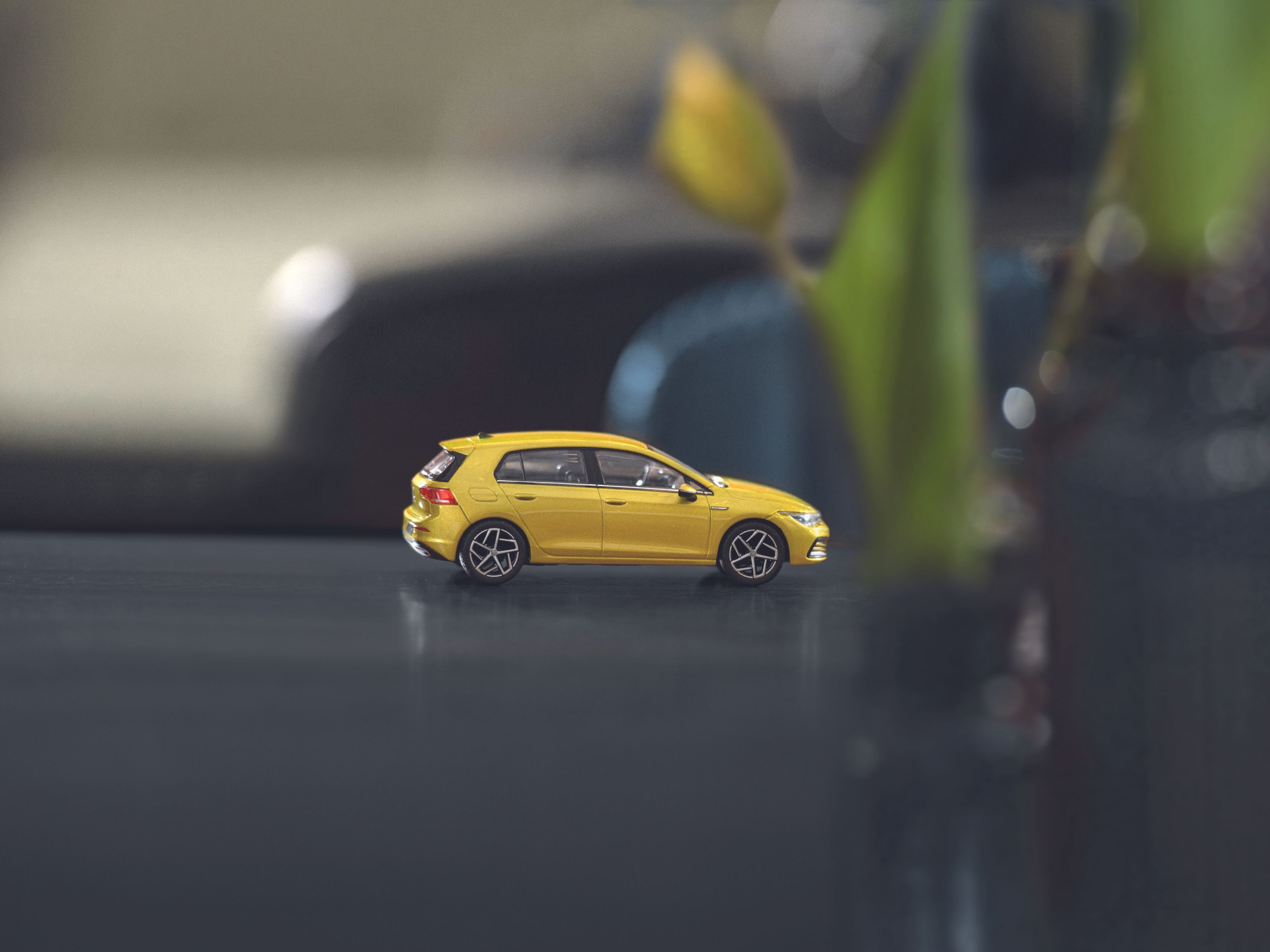 A yellow miniature Volkswagen Golf 8 model car placed on a table.