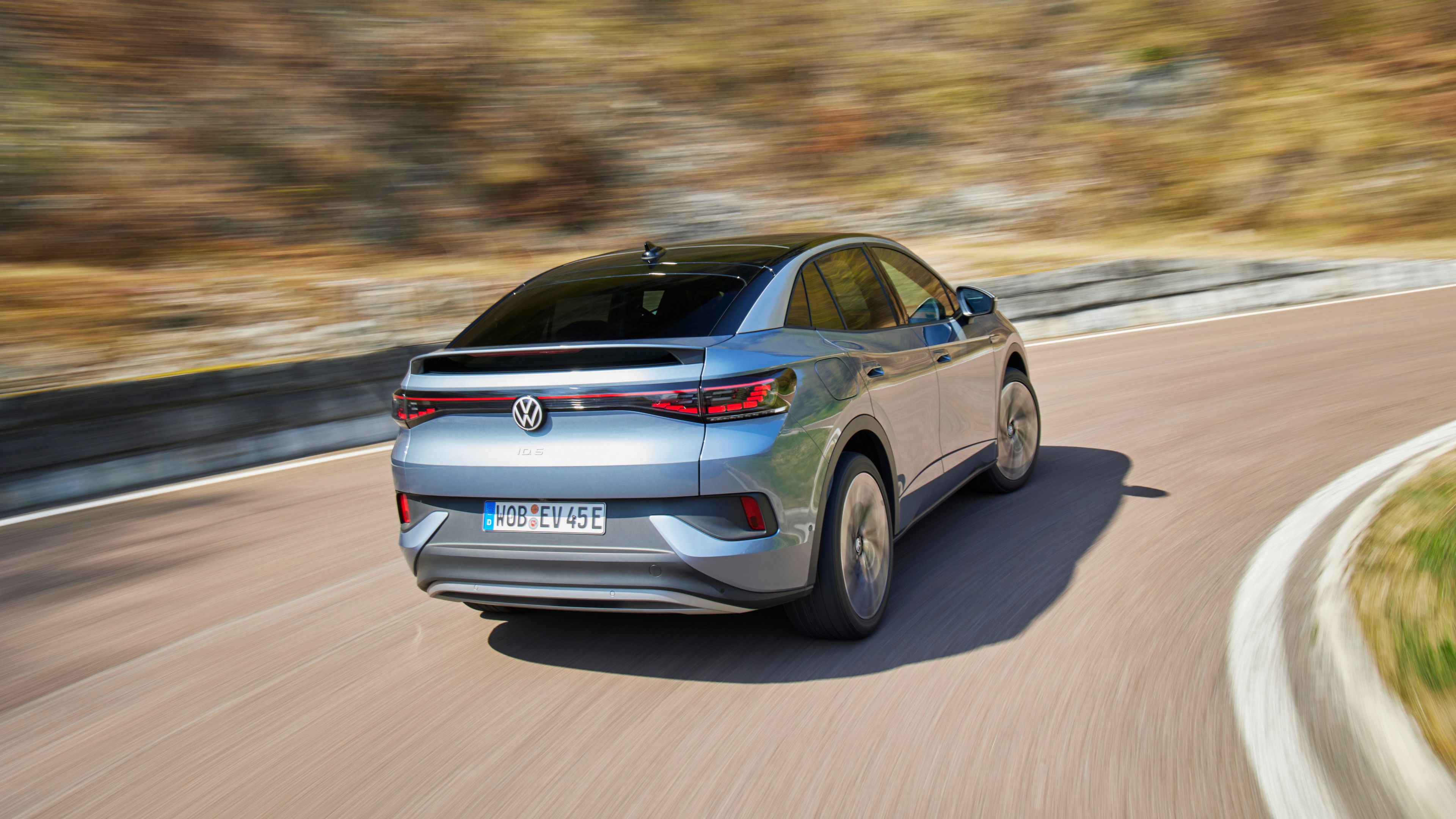 A Grey Volkswagen ID.5 rolling in fast speed on the road beside the mountain