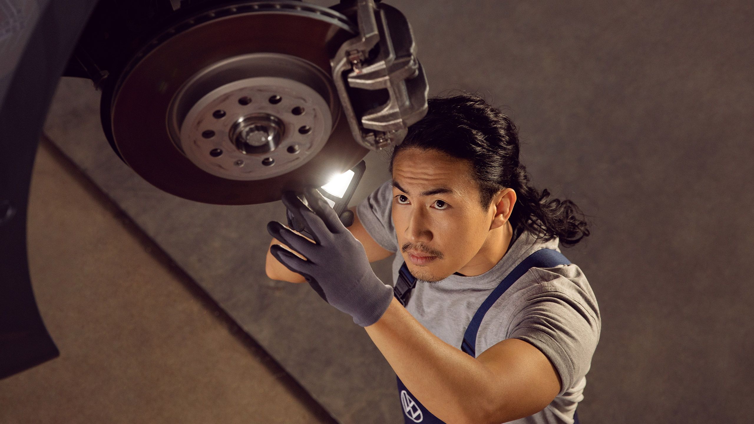 A Certified Volkswagen Staff using a torchlight to assess the condition of a Volkswagen's brake discs and pads.