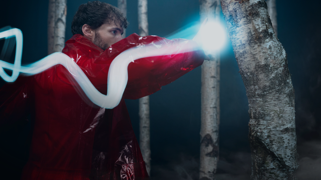 An individual dressed in striking red outfit is seen punching a tree in a studio setting.